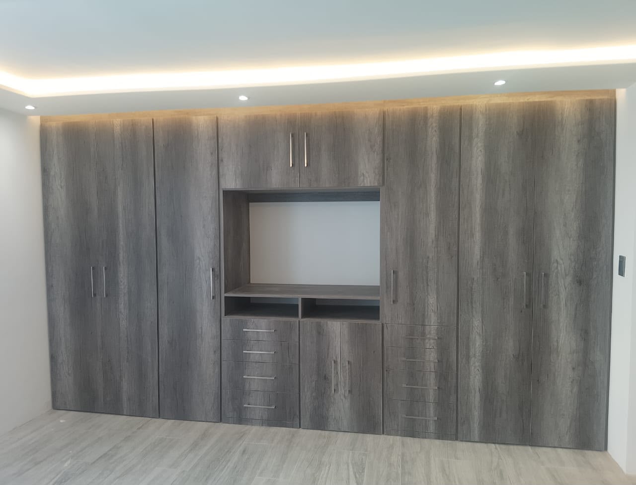 Mueble a medida en acabado gris con espacio para televisión y almacenamiento
